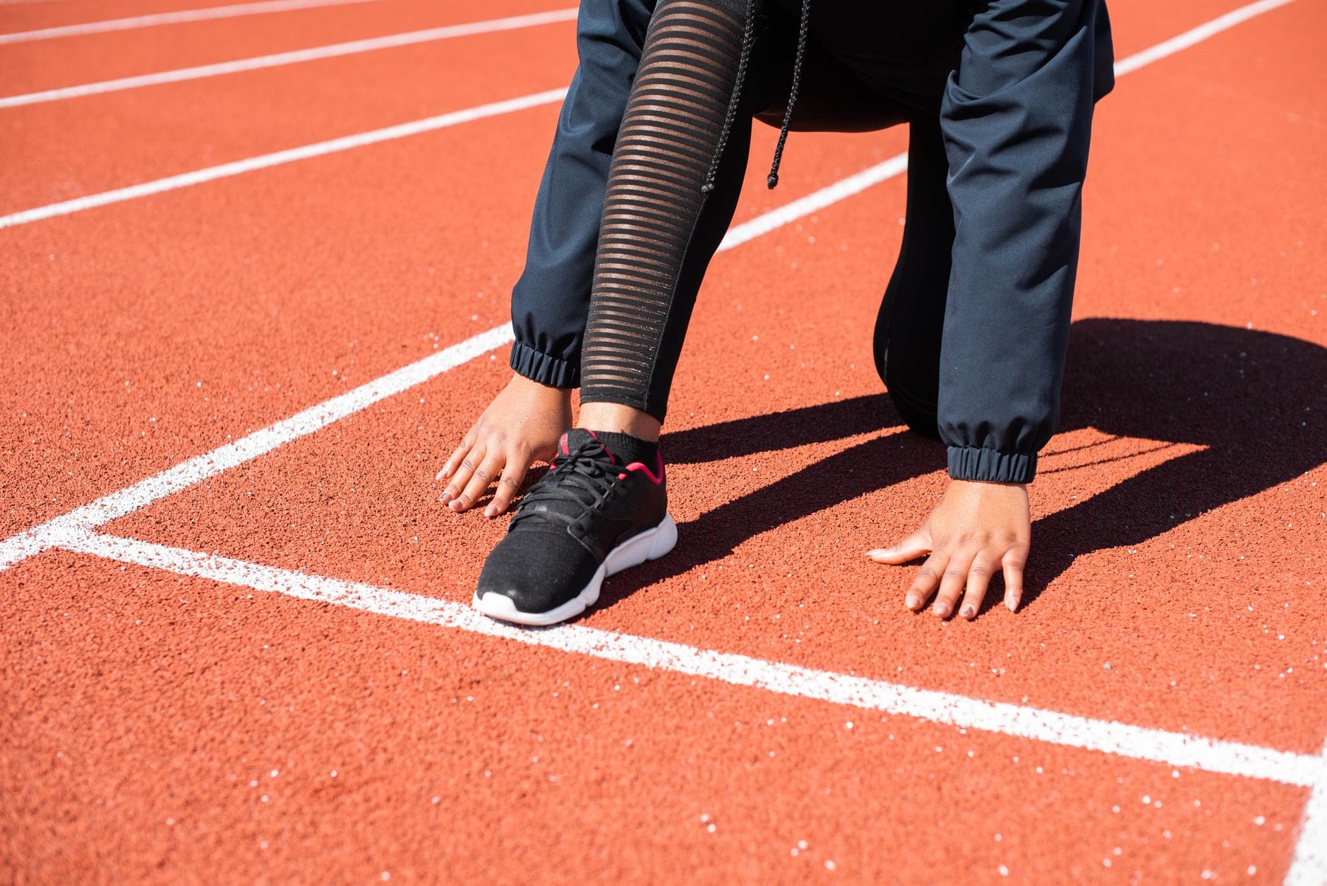 Close-up of a runner crouching at the starting line on an outdoor track.