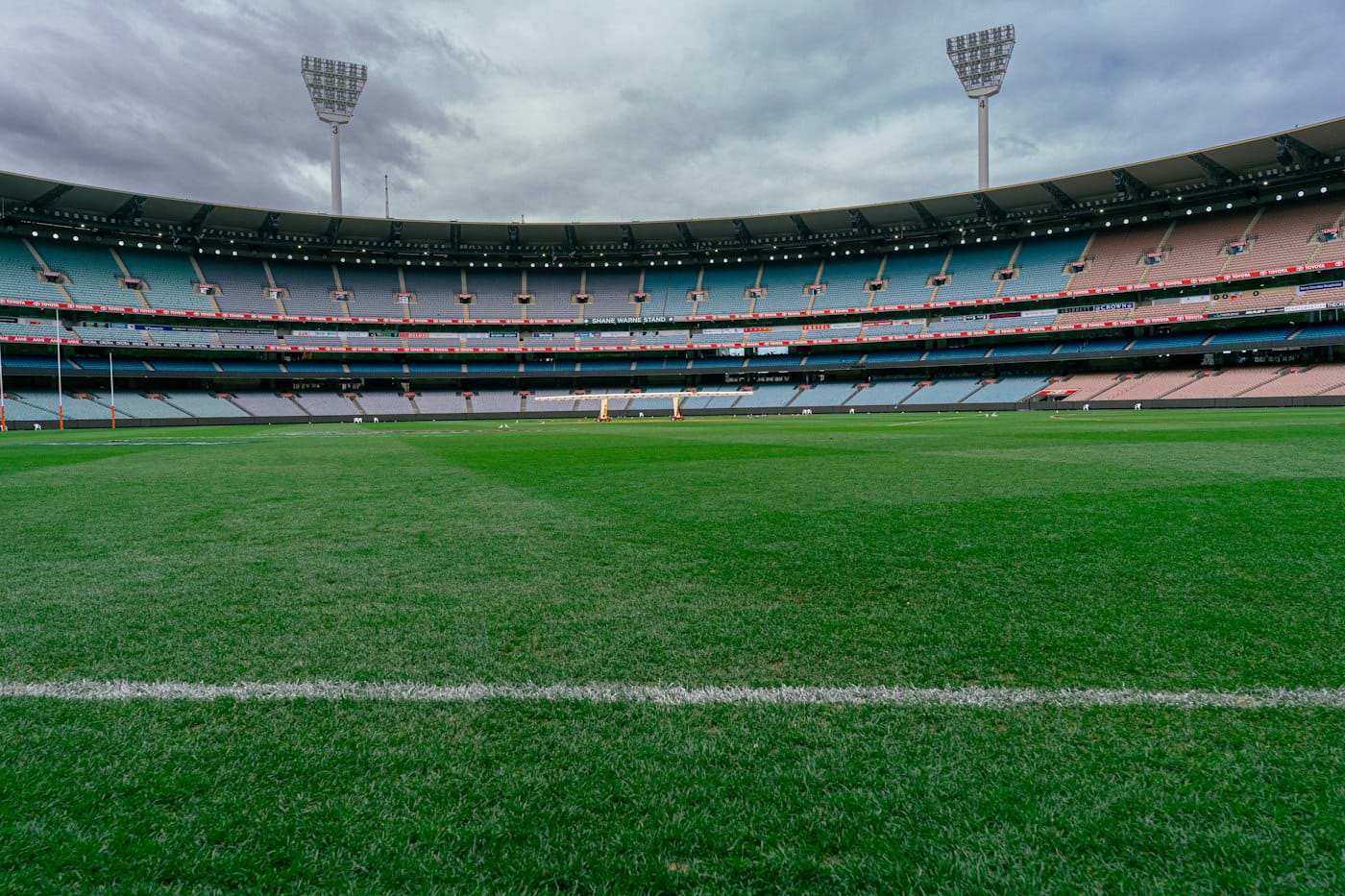 The Melbourne Cricket Ground with empty tiered seating under a cloudy sky in Melbourne