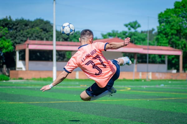 Athlete performs a flying kick in a soccer match on a sunny day in Hà Nội, Vietnam.